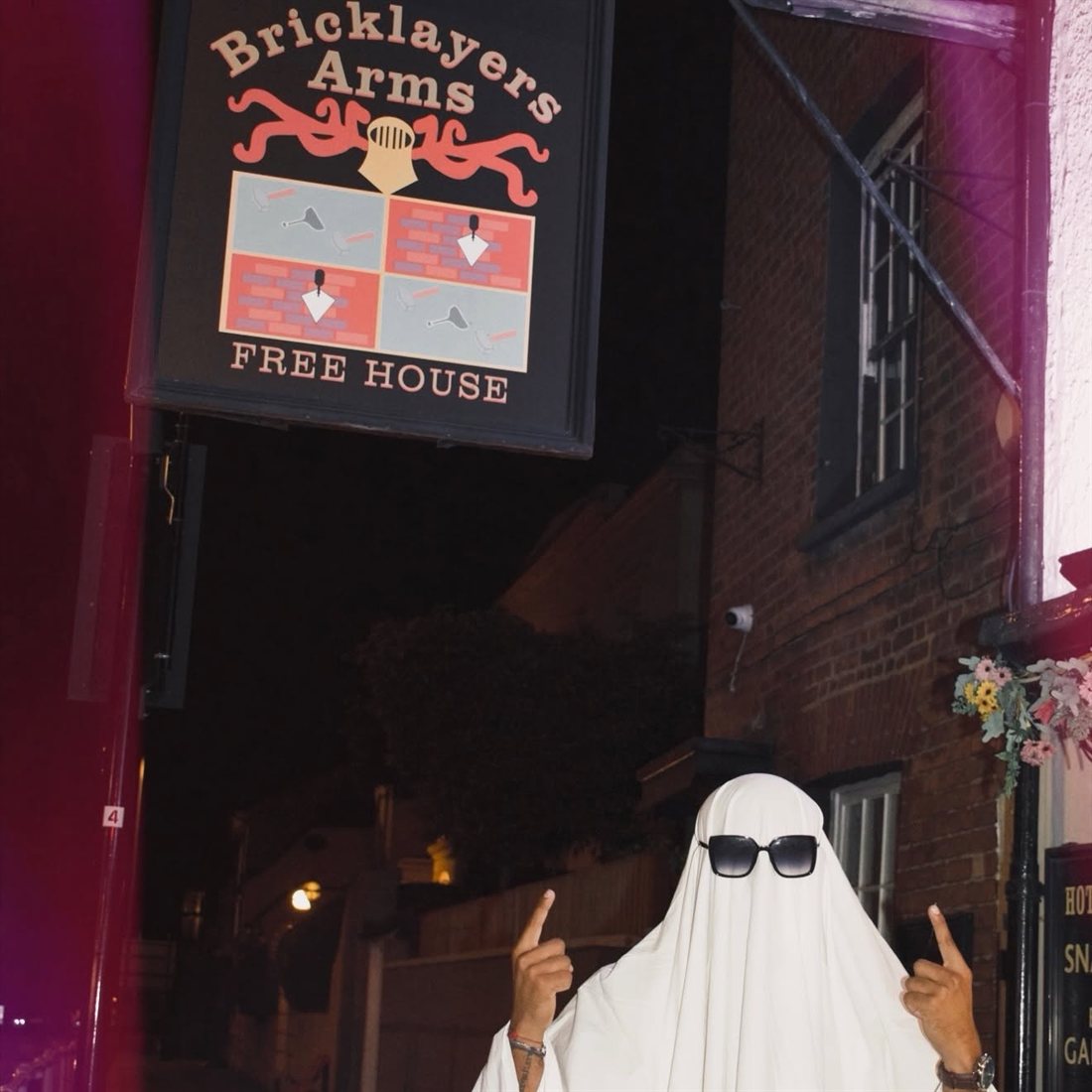 The Bricklayers Arms Free House sign at night, with the Brickies ghost in sunglasses underneath